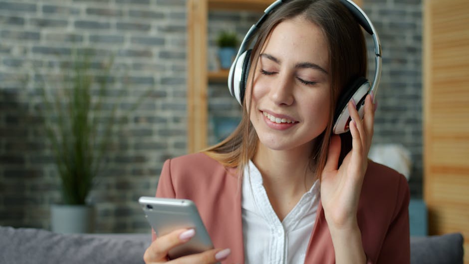 İç mekanda kulaklıkla müzik dinleyen ve akıllı telefonuyla oynayan gülümseyen bir kadın.